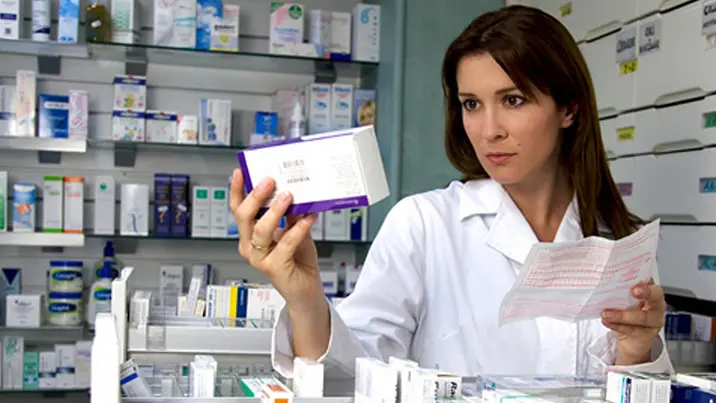 Beautiful female model pharmacist looking at medicine