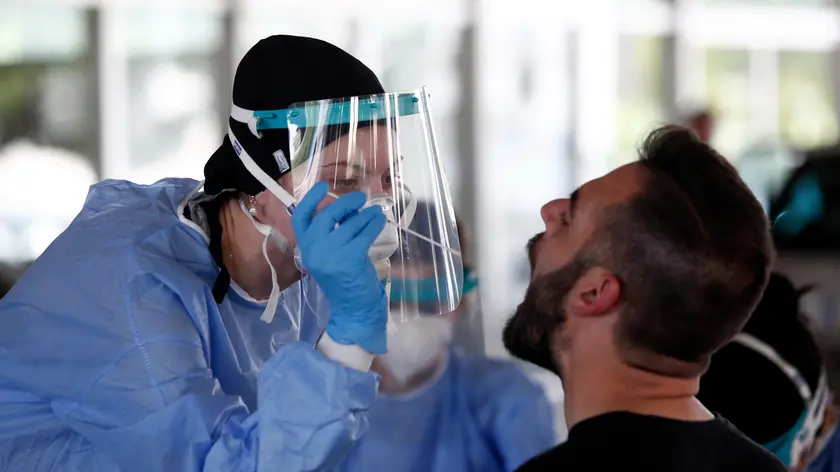 A health worker wearing protective gear takes swab samples from a tourist to test for the coronavirus, at Promahonas border crossing with Bulgaria, which is the only land border into Greece that is open on Monday, July 6, 2020. Dozens of vehicles of Serb holidaymakers who were trapped at the Greek border overnight have been allowed to cross into Greece after a ban on the entry of people from Serbia came into effect due to a coronavirus flare-up in Serbia. (AP Photo/Giannis Papanikos)