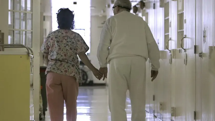 FILE - In this Wednesday, April 9, 2008 file photo, Debbie Coluter, a certified nursing assistant, holds the hand of an elderly inmate with Alzheimer's disease, as she helps him to his cell at the California Medical Facility in Vacaville, Calif. (AP Photo/Rich Pedroncelli)