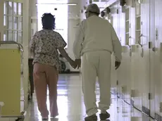FILE - In this Wednesday, April 9, 2008 file photo, Debbie Coluter, a certified nursing assistant, holds the hand of an elderly inmate with Alzheimer's disease, as she helps him to his cell at the California Medical Facility in Vacaville, Calif. (AP Photo/Rich Pedroncelli)
