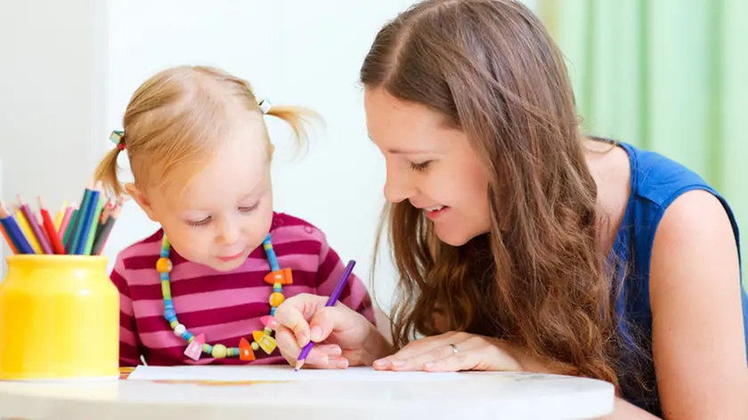 Una baby sitter aiuta una bimba a disegnare