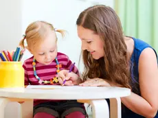 Una baby sitter aiuta una bimba a disegnare