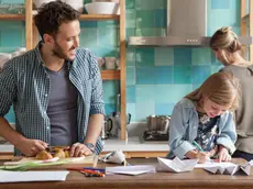 Young daughter drawing ar kitchen counter while parents prepare meal