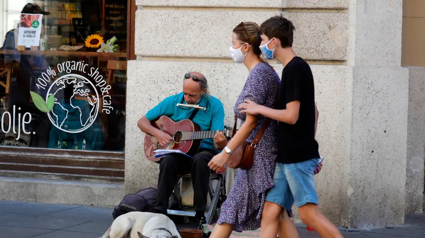 epa08628711 People with face masks pass by a street singer and his dog in Zagreb, Croatia, 27 August 2020. During the last days the pandemic of the COVID-19 coronavirus is in expansion in Croatia with more than 200 infected people on 26 August. EPA/ANTONIO BAT