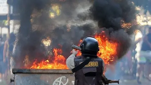 A riot police officer points his weapon toward demonstrators on the other side of a burning barricade near the Arena Fonte Nova stadium in Salvador, Brazil, Saturday, June 22, 2013. Demonstrators once again took to the streets of Brazil on Saturday, continuing a wave of protests that have shaken the nation and pushed the government to promise a crackdown on corruption and greater spending on social services. (AP Photo/Andre Penner)