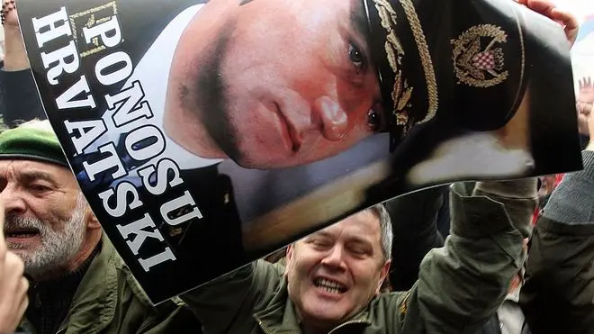 epa03473090 A man holds a poster showing a portrait of general Ante Gotowina with a slogan: 'Croatian Pride' as Croatians react on the The Hague judgment the International War Crimes Tribunal for the former Yugoslavia (ICTY) of deliberating Croatian generals Ante Gotovina and Mladen Markac, as they watch a courtroom broadcast on a screen in downtown Zagreb, 16 November 2012. The appeals chamber of the ICTY on 16 November overturned guilty verdicts against Croatian generals Ante Gotovina and Mladen Markac. The generals, who had been sentenced by the ICTY to 24 and 18 years respectively on charges of war crimes and crimes against humanity, were to be released immediately. Croatia hailed the verdict and street celebrations erupted immediately after it was read. EPA/ANTONIO BAT