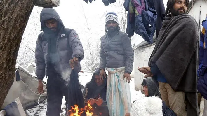 epa08043985 Migrants warm themselves by the fire in front their tent during a snowy winter day at the Vucjak refugee camp outside Bihac, northwestern Bosnia and Herzegovina, 04 December 2019. Hundreds of migrants remain at the camp even after international officials called for it to be shut down due to lack of facilities. EPA/FEHIM DEMIR