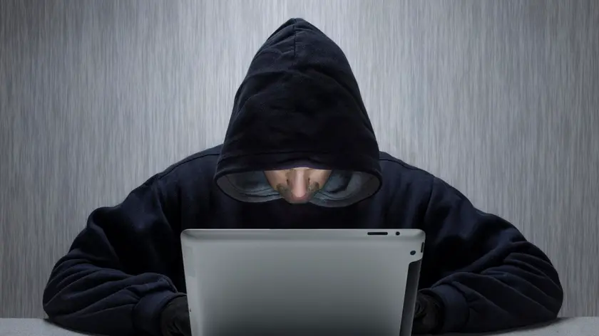 Wales, Monmouthshire, Monmouth. An anonymous hooded male using a tablet computer to represent a cyber criminal.