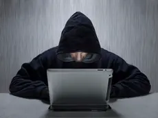 Wales, Monmouthshire, Monmouth. An anonymous hooded male using a tablet computer to represent a cyber criminal.