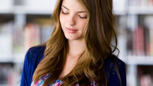 Young woman reading text message on smart phone in library --- Image by © Jim Craigmyle/Corbis